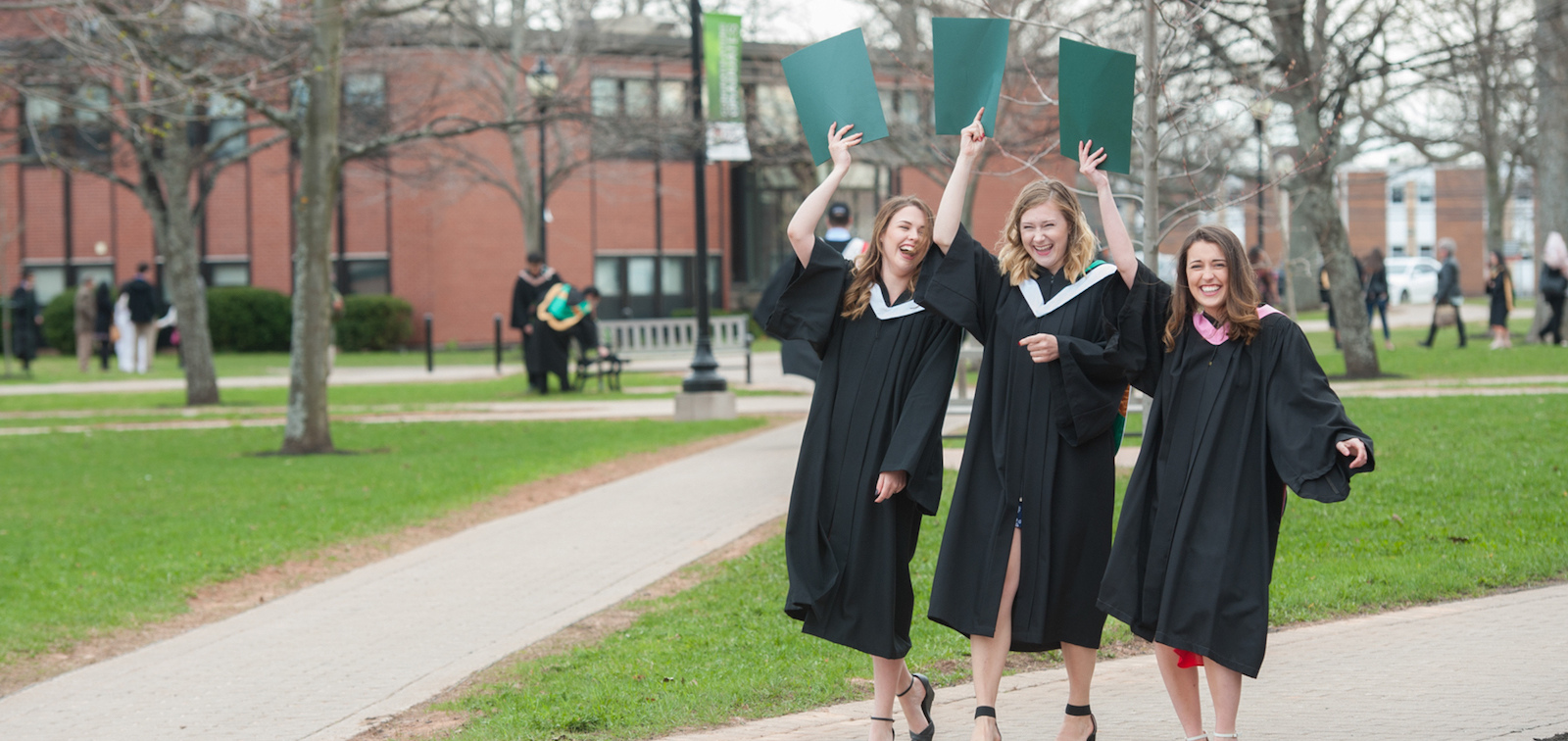 three BCA graduates holding degrees in the quadrangle