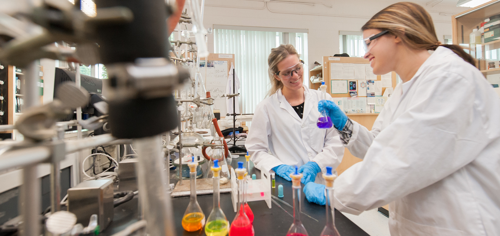 two chemistry students in laboratory with coloured flasks 