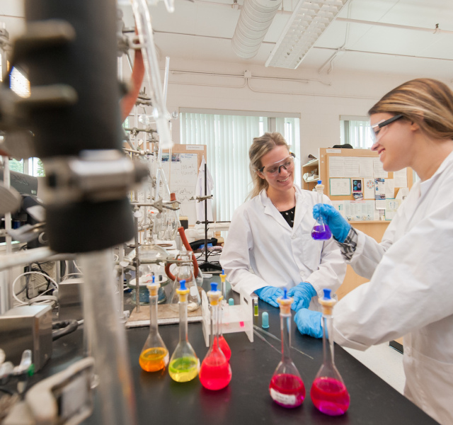 two chemistry students in laboratory with coloured flasks 